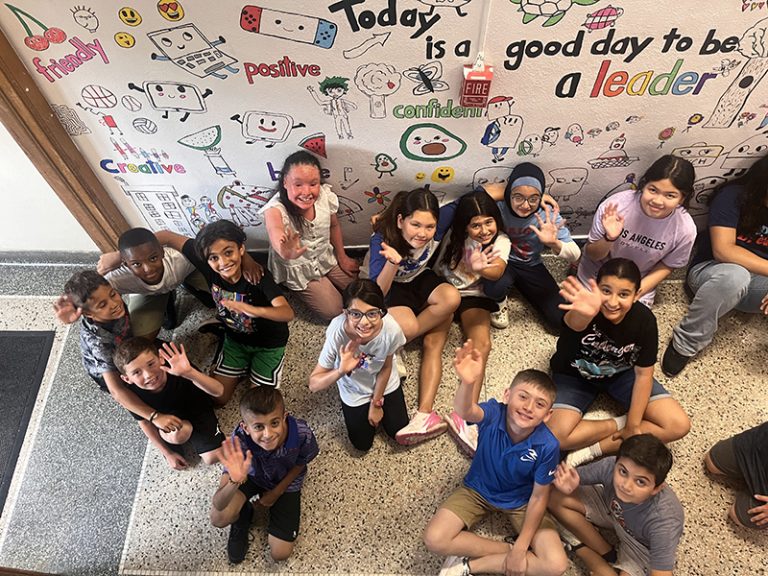 A group of students poses in front of a mural they are creating during the 2024 Summer Discovery Program at Lindbergh Elementary.